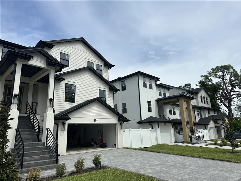 White two-story homes with black window trim and a paver driveway