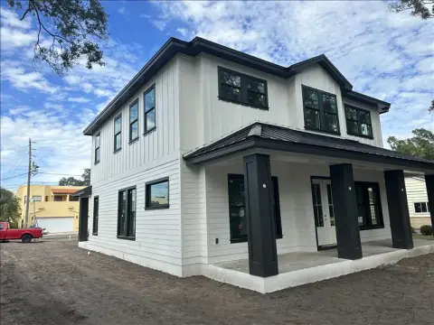 Two-story white farmhouse-style home with black columns and a covered porch, freshly painted exterior