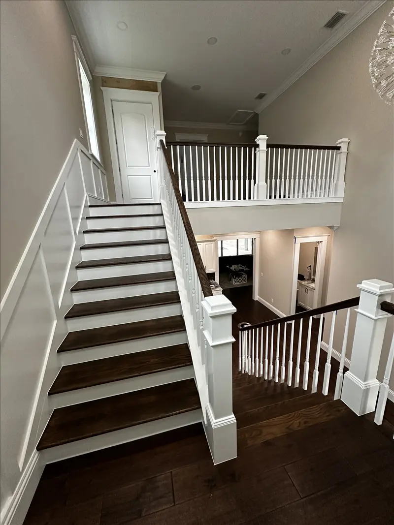 Staircase with white painted railings, wainscoting and dark stained treads