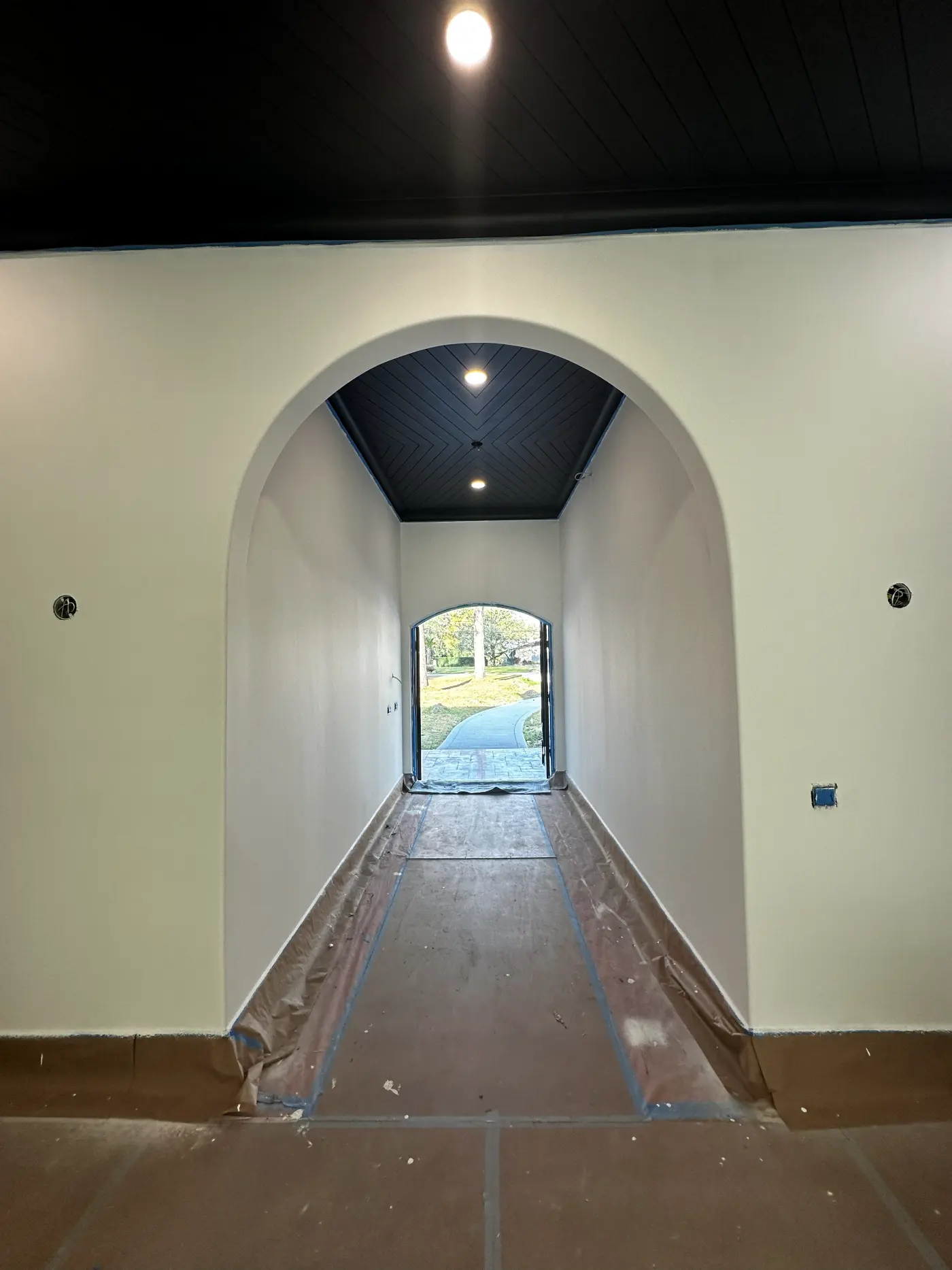 White arched hallway with a dark ceiling and a view to the entry