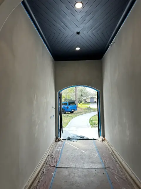 Long entry corridor with limewash walls and a dark chevron-pattern ceiling